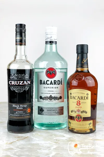 three liquor bottles on table top for rums used in a pina colada. Cruzan blackstrap bottle, bacardi light bottle and a bacardi 8 bottle.