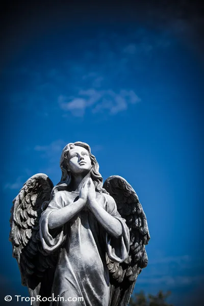 Angel Statue with praying hands with blue sky above it.