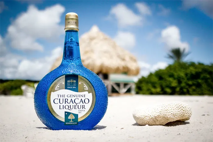 The authentic blue Curacao Liqueur bottle on the beach made from the Lahara fruit.