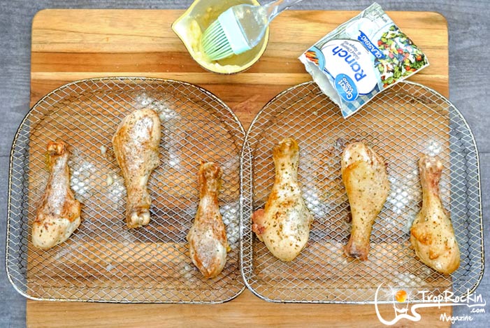 Cooked Chicken Legs on the air fryer racks with Ranch dressing sprinkled over the top.