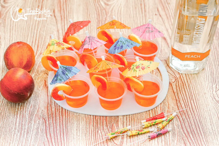 Peach jello shots with drink umbrellas on serving tray with vodka botle in the background.