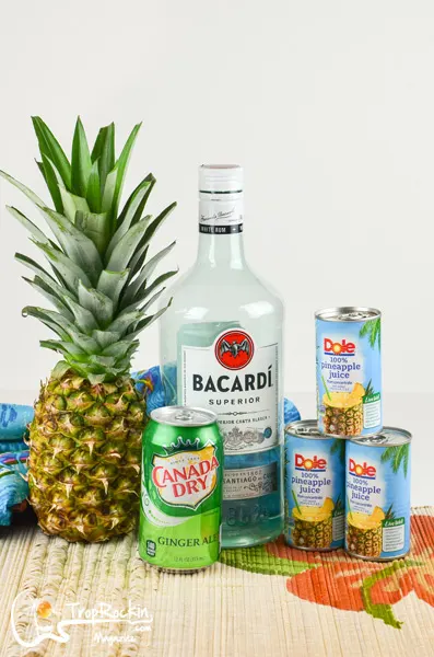 Pineapple Rum Punch ingredients: Pineapple, Rum Bottle, Pineapple Juice in cans and a can of ginger ale. 