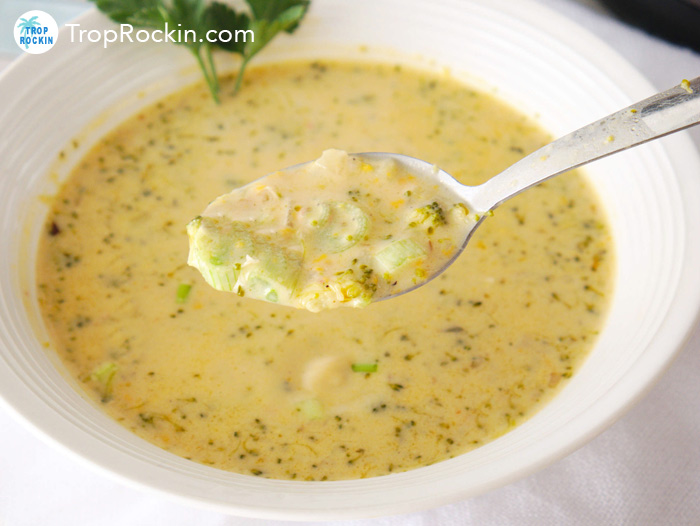 A bowl of cream of broccoli cheese soup and a spoon full of soup above the bowl.