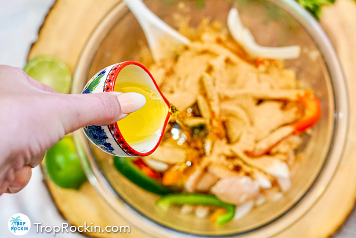 Pouring olive oil into bowl of raw chicken, peppers and onions.
