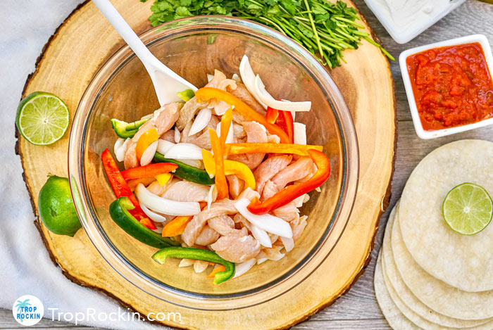 Mixing bowl filled with raw chicken, sliced peppers and onions.