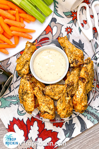 Air Fryer Lemon Pepper Wings displayed on a clear plate with ranch dressing, baby carrots and celery sticks.