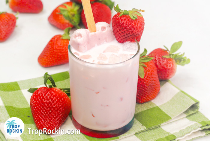 Strawberries and Cream Drink with ice cream popsicle dipped inside and fresh strawberries around drink glass.