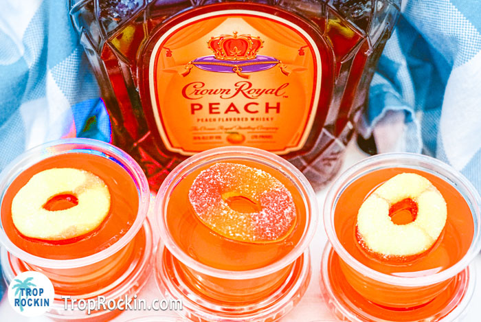 Peach Crown Jello Shots with peach rings on top with a bottle of Peach Crown in the background.