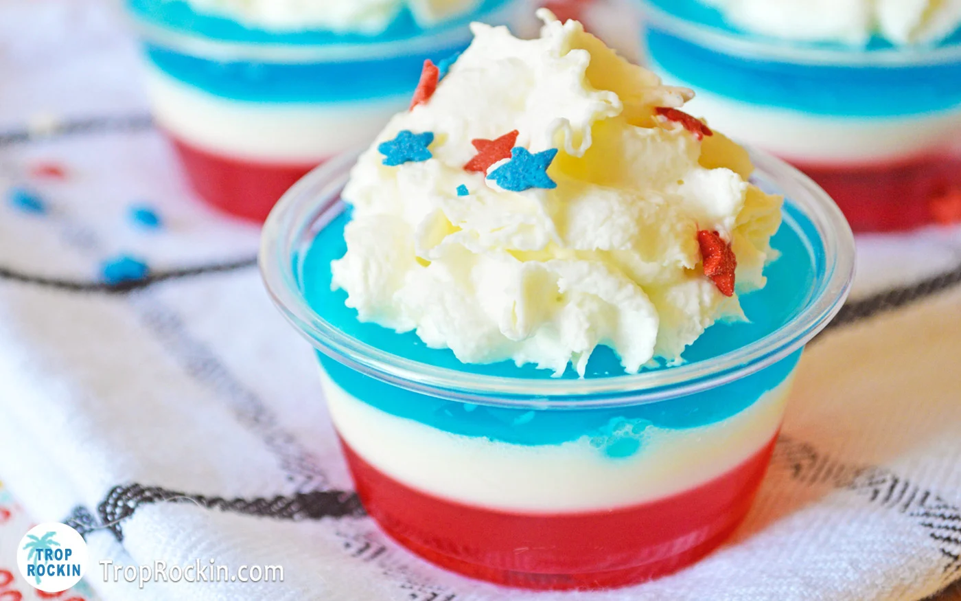 Red White and Blue Jello Shots on table with Whipped Cream and star shaped sprinkles on top.