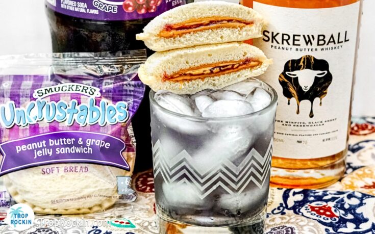 Skrewball Peanut Butter and Jelly Drink with mini PB&J sandwiches for garnish with Skrewball Peanut Butter Whiskey bottle in the background.