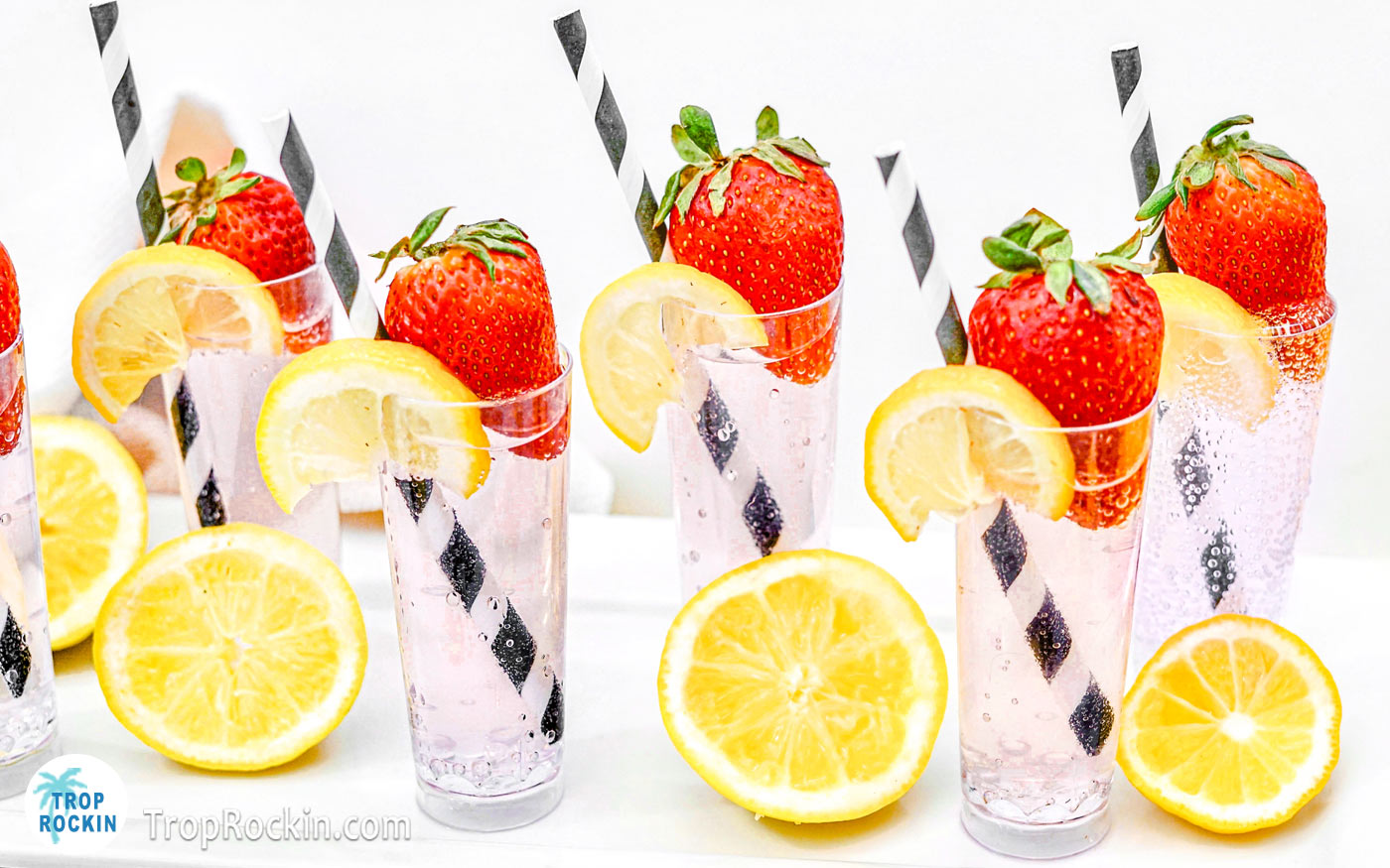 Strawberry Lemonade Vodka Shots lined up on a white serving tray with strawberries and lemon wedge garnish.