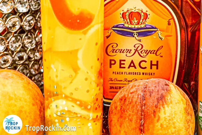 Upclose view of crown peach drink with fresh peaches and bottole of crown peach in background.
