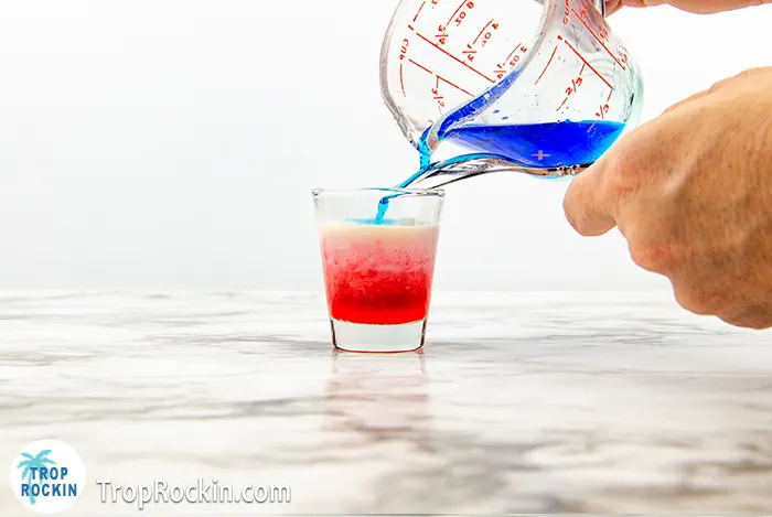 Pouring Blue Curacao on top of the Crown Peach layer to create the red white and blue layered shots look.