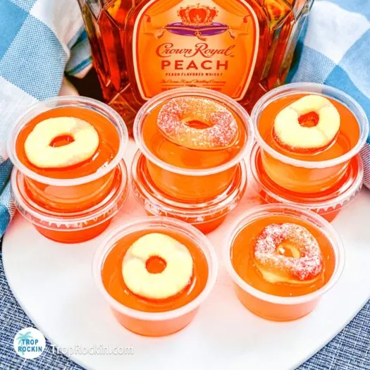 Crown peach jello shots with peach rings for garnish on top with a bottle of Crown Royal Peach Whisky in the background.