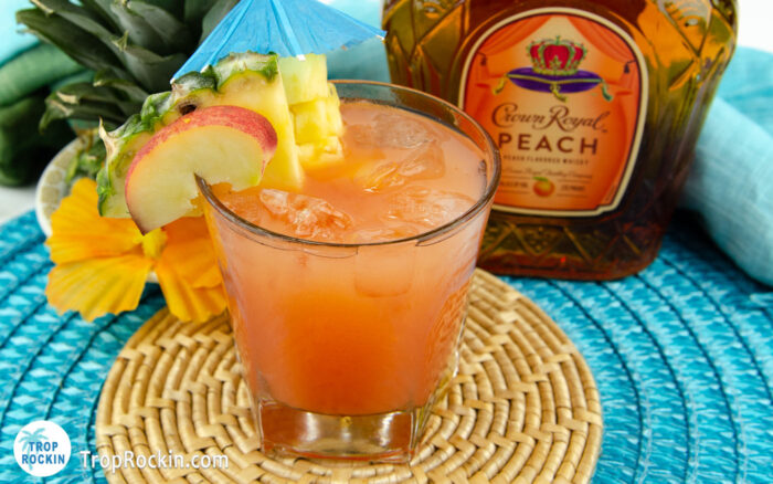 Crown Royal Peach Beach Drink with crown peach bottle and tropical flowers in the background.