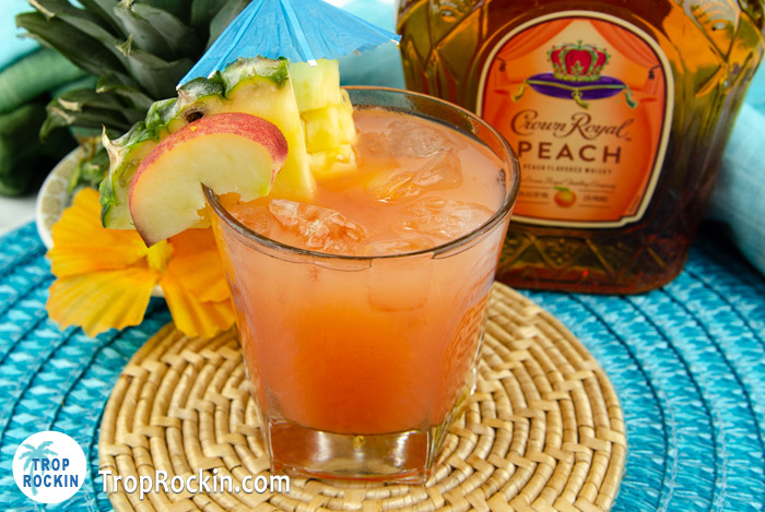 Crown Royal Peach Beach Drink with crown peach bottle and tropical flowers in the background.
