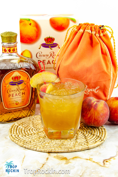 Crown Peach Whiskey bottles, fresh peach fruit and mixed drink on table.