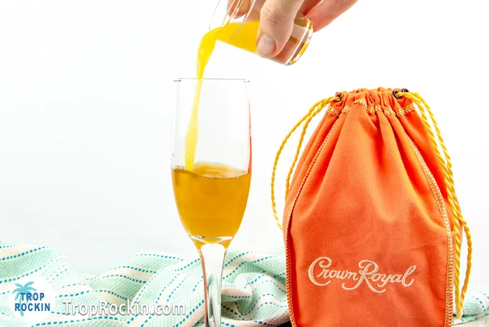 Pouring orange juice over Crown Royal Peach Whisky in a champagne glass.
