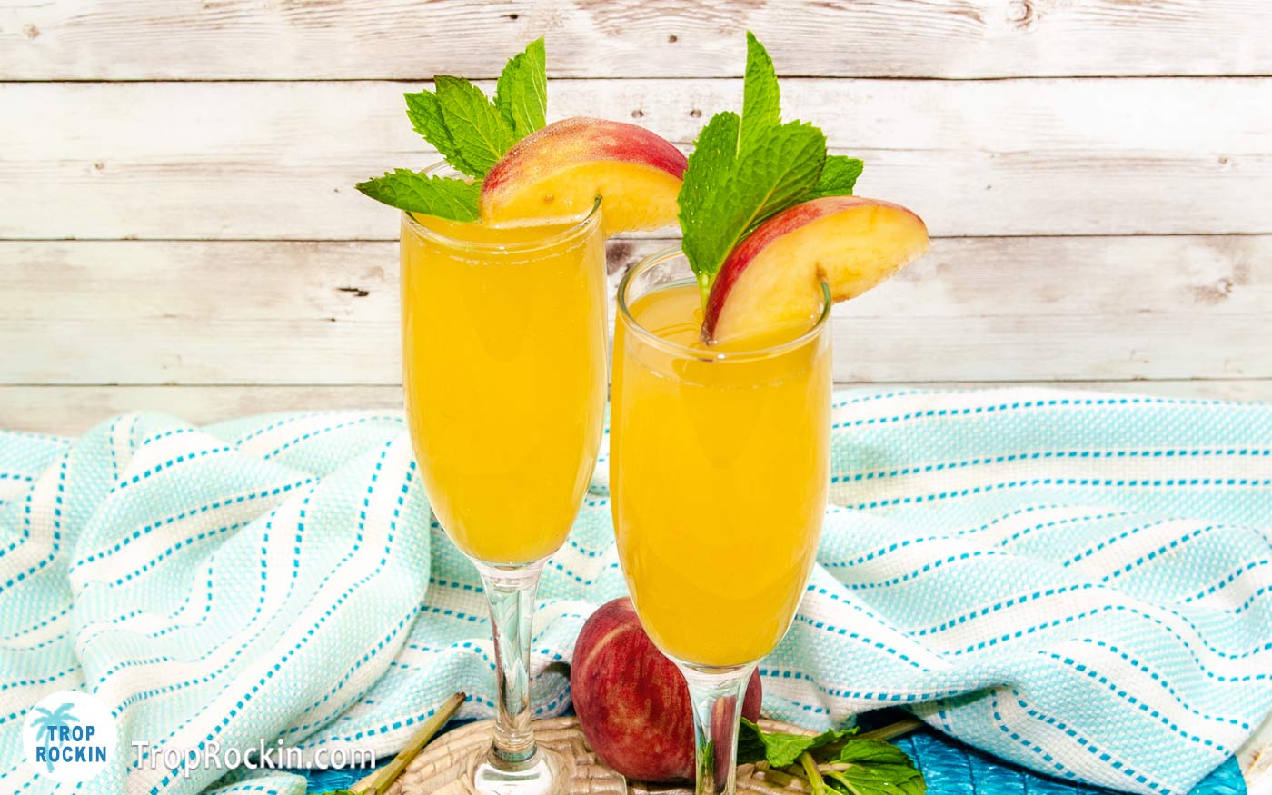 Two glasses of Crown Royal Peach Mimosa drink with peach slices and mint sptrig for garnish.