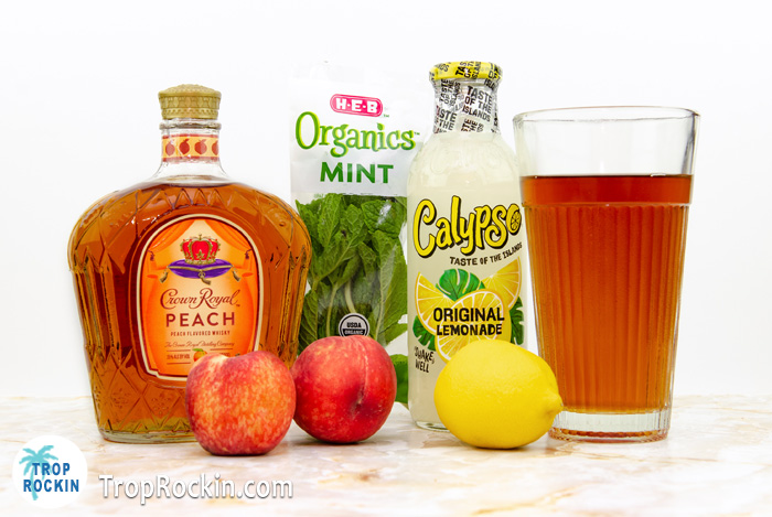 Bottle of Crown Peach whisky, glass of brewed tea, Bottle of Lemonade, fresh peach and mint.