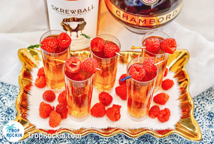 peanut butter and jelly shots with raspberries on a skewer with Skrewball Whiskey bottle and Chambord bottle. 