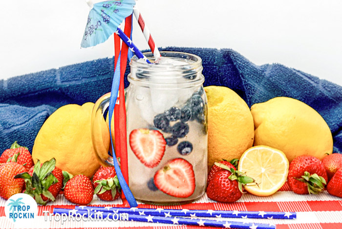 Red white and berry cocktail with fresh lemons, strawberries and blueberries on a red and white checkered placemat. 