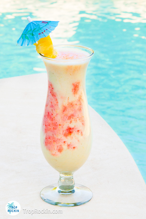 Summer Cocktail Recipes: The Lava Flow drink in a hurricane glass with swimming pool in the background.