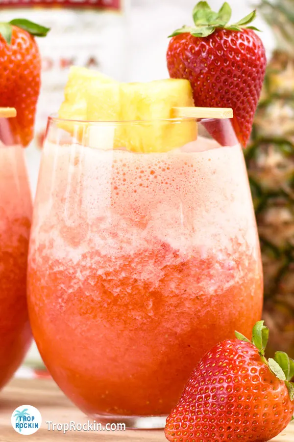 A cocktail glass of Pineapple Strawberry Lemonade Vodka Slush with fresh strawberries and pineapple chunks for garnish.