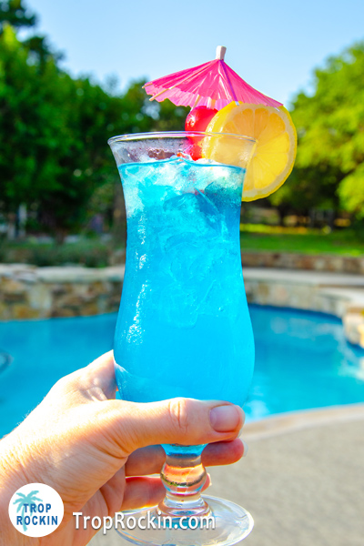 Holding the Blue Lagoon cocktail with a swimming pool in the background.