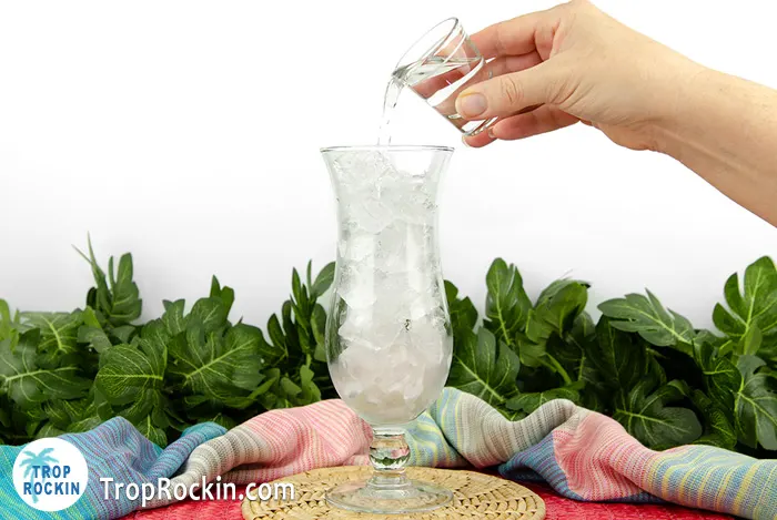 Pouring Vodka into hurrican glass filled with ice.