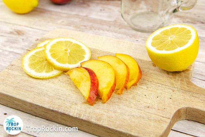 Fresh peach slices and a sliced lemon on cutting board.
