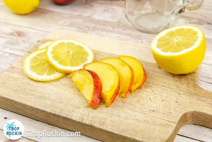 Fresh peach slices and a sliced lemon on cutting board.