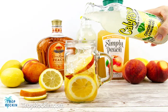 Pouring lemonade over the Crown Peach and peach juice in a mason jar glass.