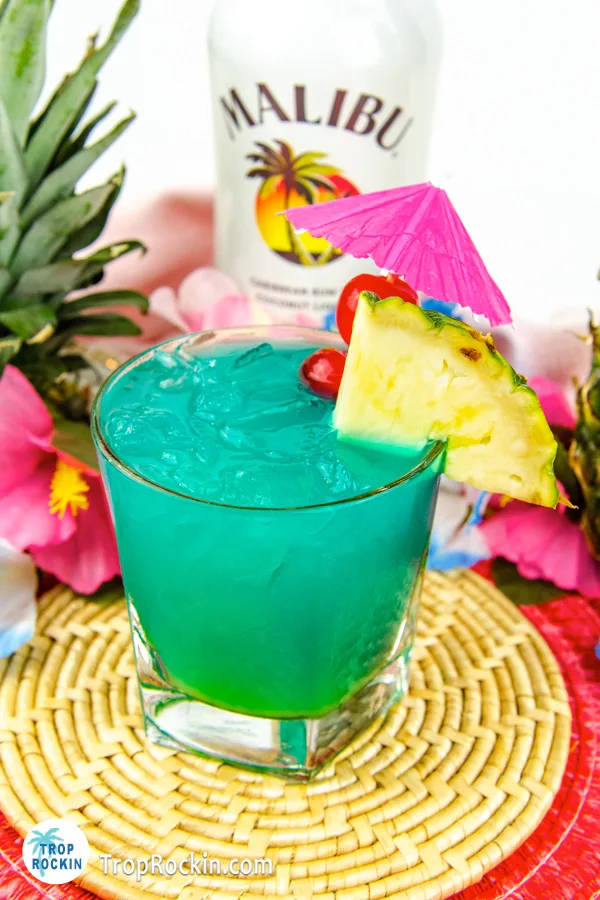 Malibu Rum drink, the Electric Smurf, with pineapple slice and cherries for garnish with bottle of malibu rum in the background.