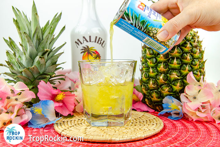 Pouring pineapple juice into cocktail glass on top of Malibu coconut rum. 
