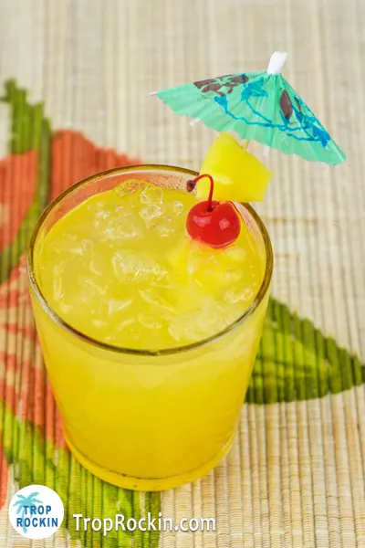 Pineapple rum punch tropical drink with a cherry and pineapple chunk garnish on a bamboo style placemat.