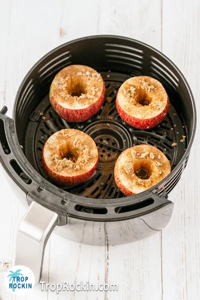 Apples cored and sprinkled with brown sugar and cinnamon in the air fryer basket.