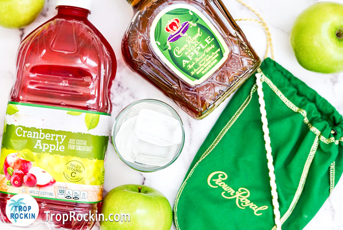 Crown Apple and Cranberry Juice bottles with a cup of ice and green apples. 