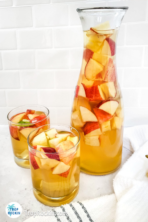 Caramel Apple Sangria with fresh fruit in a pitcher and two glasses.