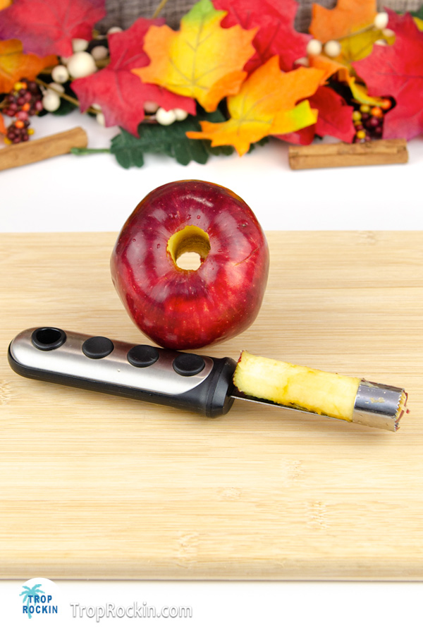 Cored red apple with apple corer on a cutting board.