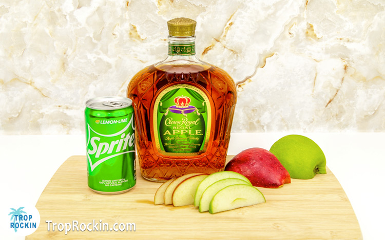 Apple Crown and Sprite drink ingredients on a cutting board. Can of Sprite, bottle of Apple Crown and green and red apple slices. 