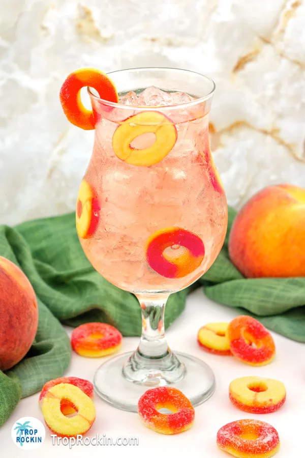 Crown Royal Peach Ring Drink with peach rings garnish and fresh peaches on counter top.
