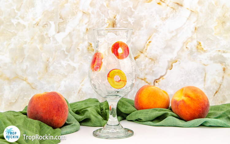 Hurricane glass with ice and several peach rings inside the glass.