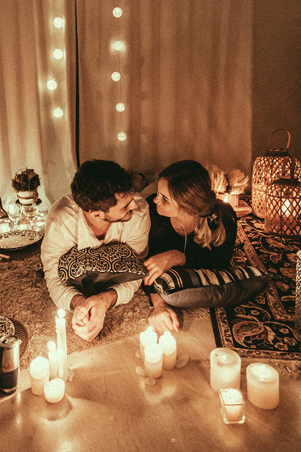 Couples Staycation Ideas: Couple having a romantic picnic indoors with candles and fairy lights.