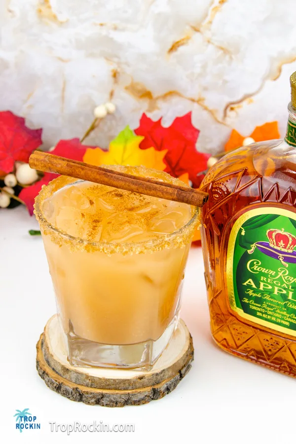 Crown Royal Caramel Apple drink with cinnamon stick on top for garnish next to a bottle of Crown Royal Apple Whisky.