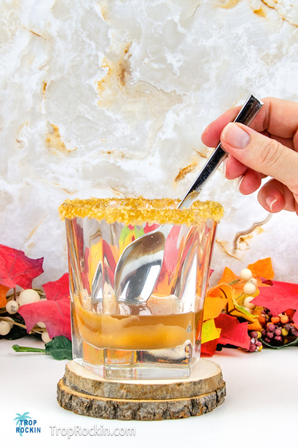 Stiring Crown Apple and caramel sauce in glass with a spoon.