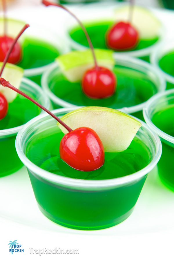 Close view of Crown Apple Jello Shots with green apple slices and Maraschino cherries for garnish.