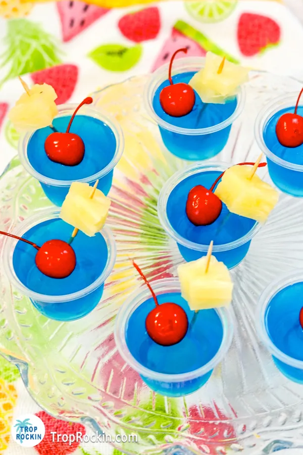 Close up photo of Blue Hawaiian Jello Shots with maraschino cherries and pineapple chunks for garnish on a serving platter.