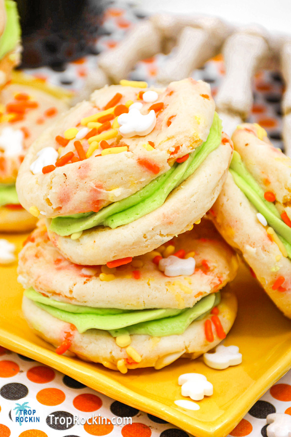 Cake Mix Cookie sandwiches with neon green frosting and sprinkles stacked on a plate.