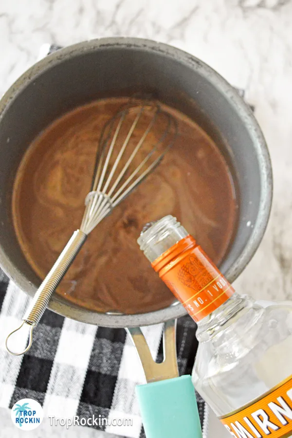 Pouring caramel vodka into the hot chocolate mixture in the pot. 